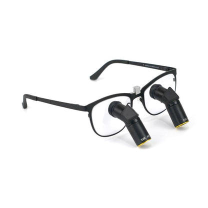 A side-angle product image of Oradenix Ergo TTL Ti Vario dental loupes featuring a sleek black titanium frame. The integrated 5.0X magnification lenses are designed with a downward ergonomic angle to prevent neck strain. The lens barrel clearly shows the "5.0X" marking and the variable focus mechanism, ideal for high-precision endodontic and restorative dental procedures.