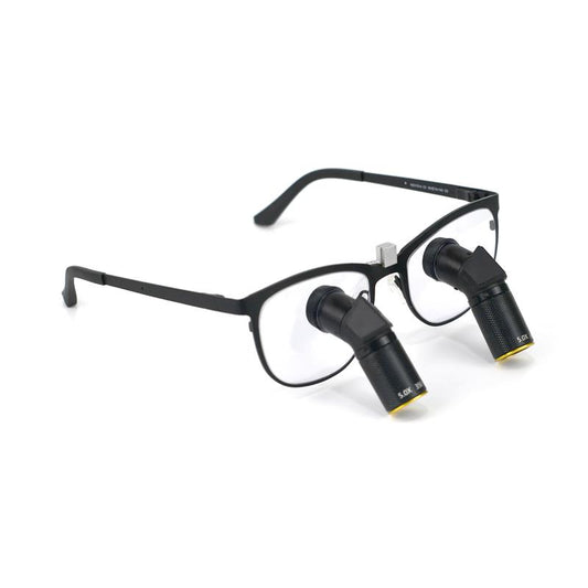 A side-angle product image of Oradenix Ergo TTL Ti Vario dental loupes featuring a sleek black titanium frame. The integrated 5.0X magnification lenses are designed with a downward ergonomic angle to prevent neck strain. The lens barrel clearly shows the "5.0X" marking and the variable focus mechanism, ideal for high-precision endodontic and restorative dental procedures.