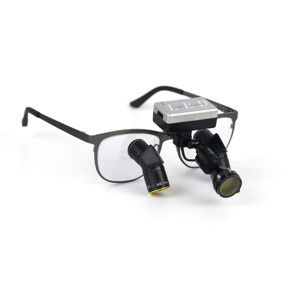 A close-up product shot of the Oradenix ProLite wireless surgical LED headlight securely mounted onto a pair of Oradenix titanium ergonomic dental loupes. The image highlights the truly cable-free design, featuring the sleek silver battery pack resting cleanly on the frame's bridge. The adjustable black lamphead is equipped with the magnetic anti-curing yellow filter, demonstrating perfect integration and balance for dental professionals.