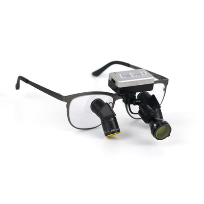 A close-up product shot of the Oradenix ProLite wireless surgical LED headlight securely mounted onto a pair of Oradenix titanium ergonomic dental loupes. The image highlights the truly cable-free design, featuring the sleek silver battery pack resting cleanly on the frame's bridge. The adjustable black lamphead is equipped with the magnetic anti-curing yellow filter, demonstrating perfect integration and balance for dental professionals.