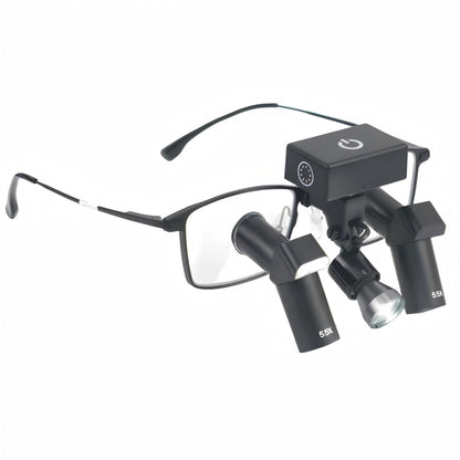 A high-resolution close-up showcasing the seamless integration of the Oradenix® wireless surgical LED headlight securely mounted on a pair of black 5.5X Ergo TTL dental loupes. The detailed view highlights the compact, rectangular touch-control battery unit resting perfectly balanced on the frame's bridge. Just below, the articulated LED lamp head is precisely aligned with the downward-angled 5.5X ergonomic deflection oculars. This setup demonstrates how the illumination path perfectly matches the clinician