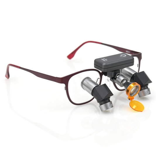 Compact wireless LED headlight mounted on ergonomic dental loupe frame featuring flip-up yellow curing filter for surgical illumination